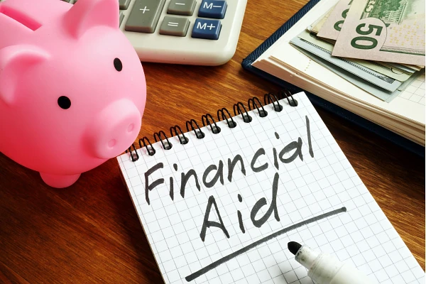 A pink piggy bank, a calculator, and a notebook with "Financial Aid" written on it are displayed on a wooden surface.